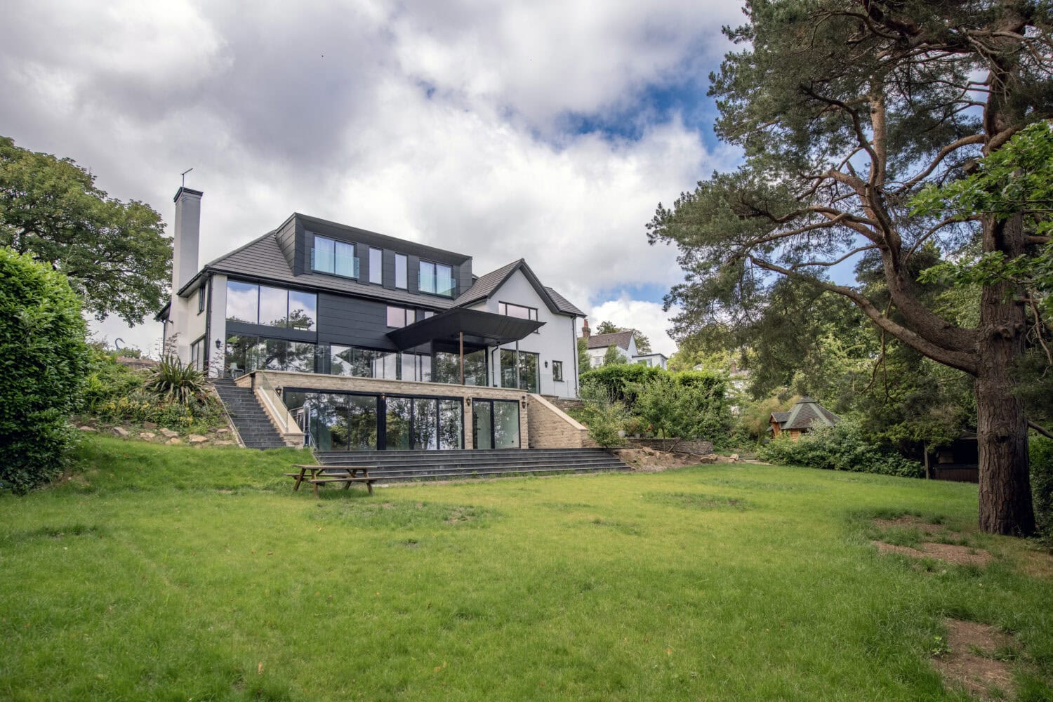 Contemporary house featuring large bi-folding doors opening to a lush green garden, showcasing modern architecture and outdoor living space.