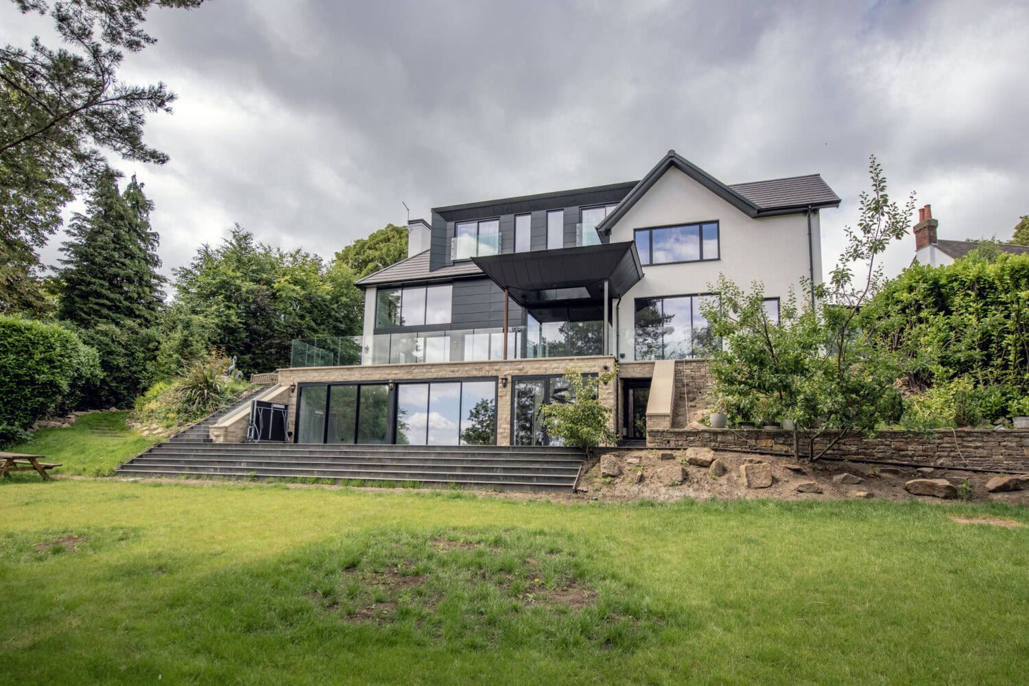 Contemporary house featuring large bi-folding doors opening to a lush garden, showcasing modern architecture and extensive glass panels for natural light.