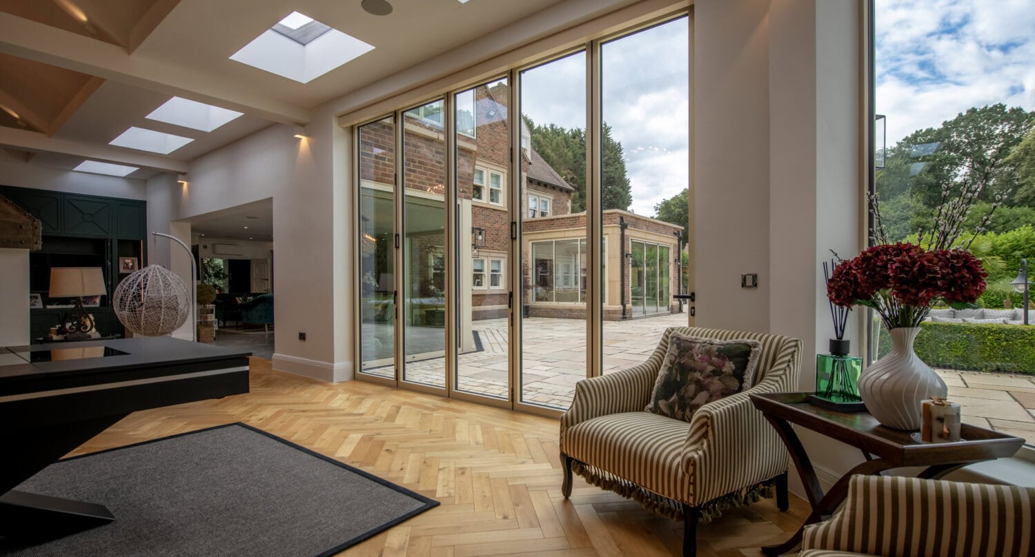 Modern interior with large glass bi-folding doors opening to garden at Foxwood House, showcasing natural light and contemporary design.