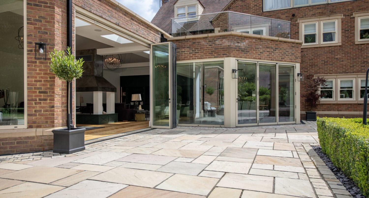 Modern bi-folding doors opening to a stylish outdoor patio at Foxwood House, showcasing seamless indoor-outdoor living with large glass panels and aluminium frames.