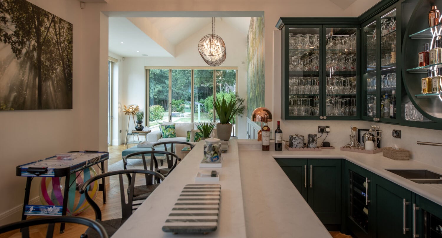 Bright modern kitchen featuring large bi-folding doors opening to a lush garden, with a white marble island and dark green cabinetry, perfect for indoor-outdoor living.