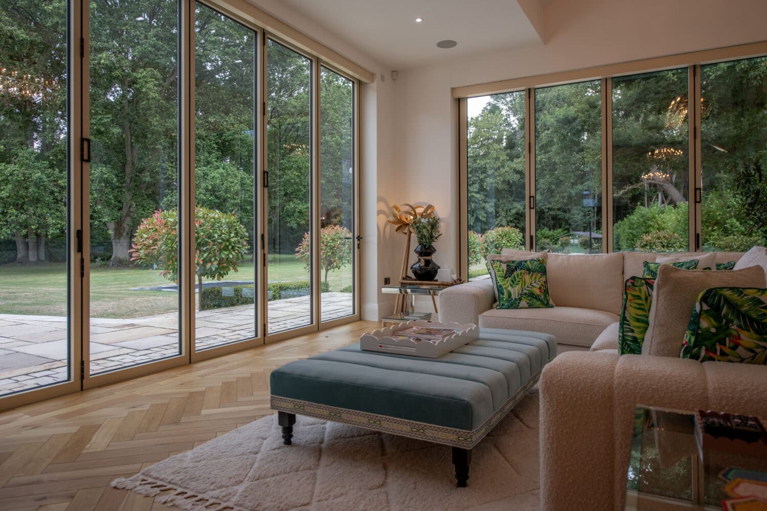 Modern living room with large glass bi-folding doors opening to a lush garden, showcasing natural light and seamless indoor-outdoor flow.