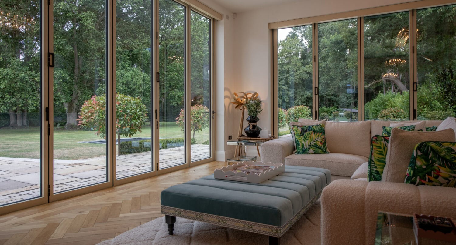 Modern living room with large glass bi-folding doors opening to a lush garden, showcasing natural light and seamless indoor-outdoor flow.
