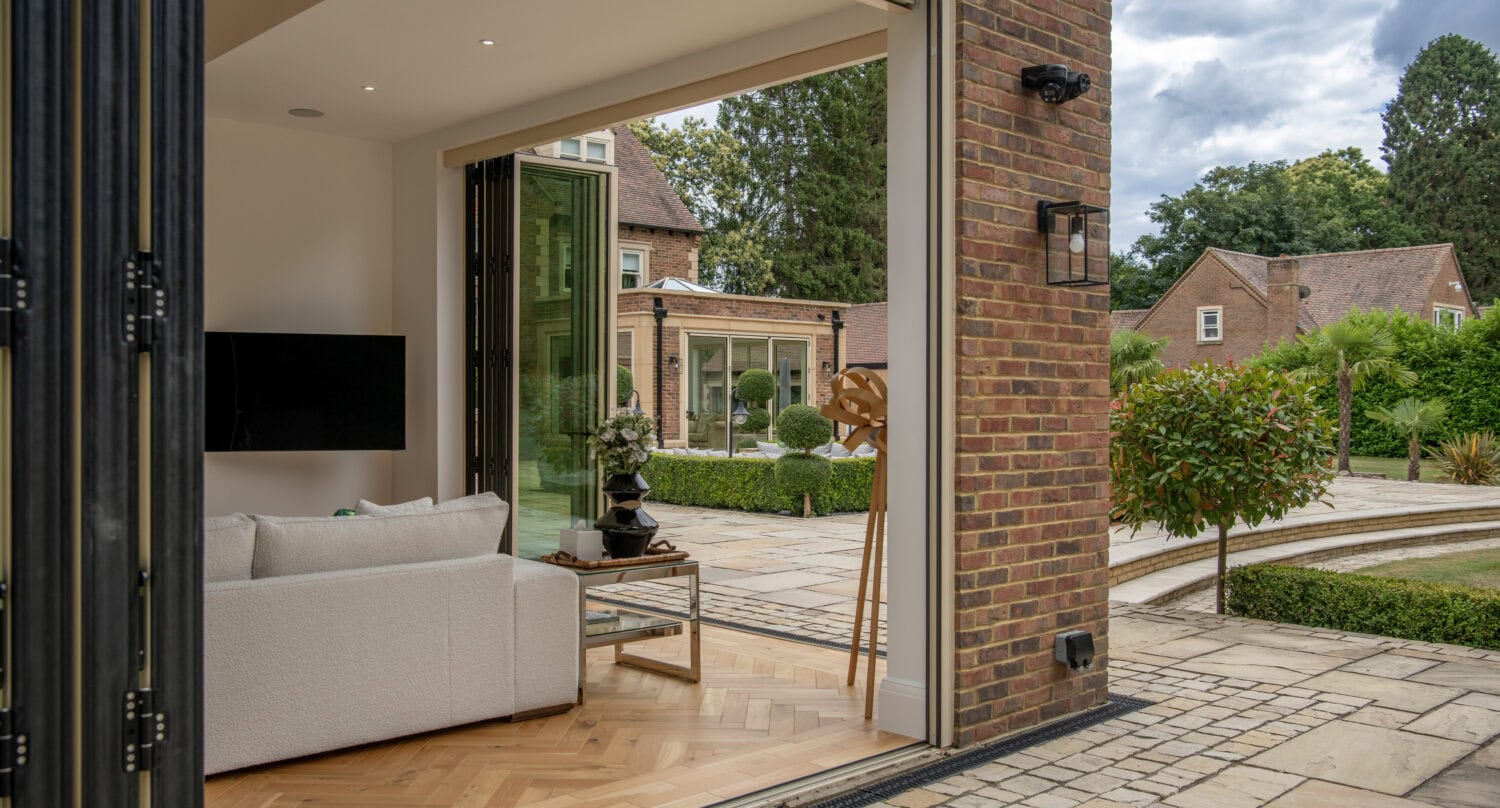 Elegant bi-folding doors opening to a stylish living room with a view of a garden, showcasing high-quality aluminium frames and seamless indoor-outdoor transition.