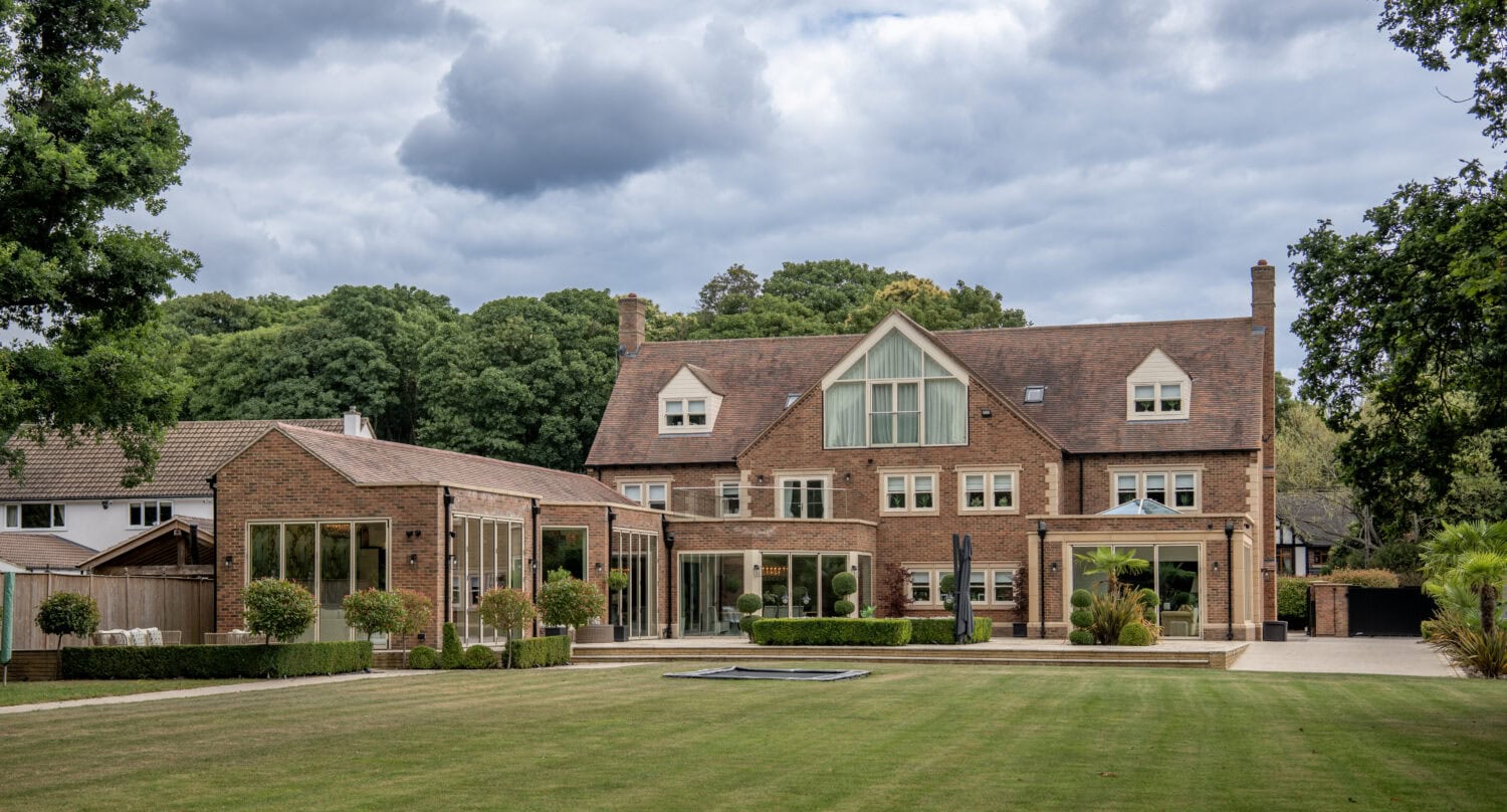 Large traditional brick house with modern bi-folding doors opening to a well-maintained garden and lawn.