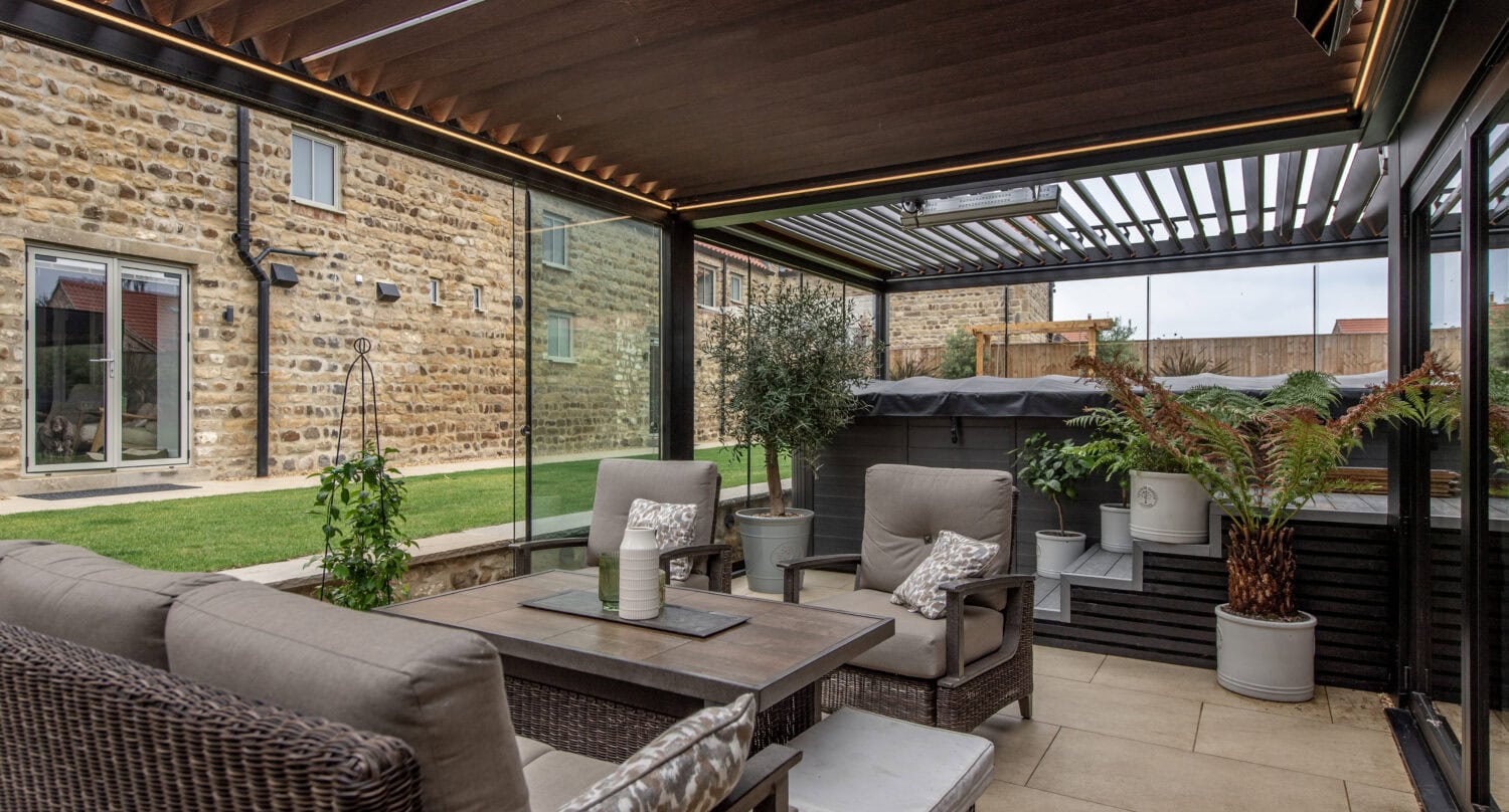 Contemporary conservatory featuring large bi-fold doors opening to a garden, with comfortable seating and lush potted plants, ideal for outdoor living.