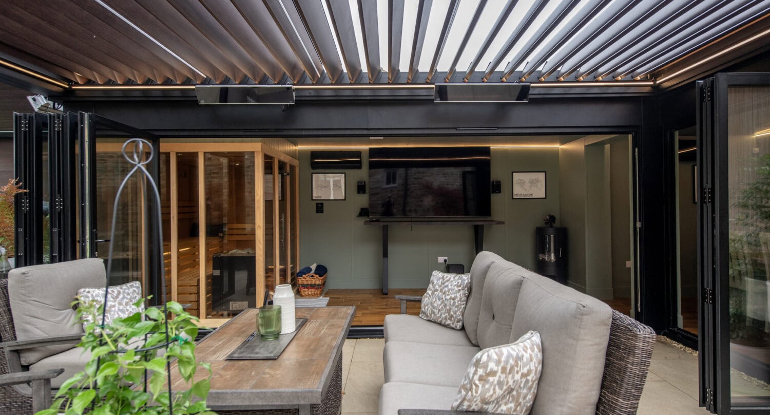 Contemporary outdoor living area featuring large bi-fold doors opening to a patio with comfortable seating and greenery.