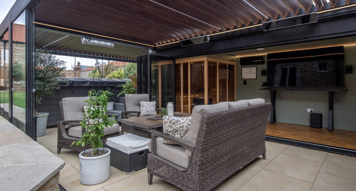 Contemporary outdoor lounge area with bi-fold doors opening to a garden, featuring comfortable seating and a wooden ceiling.