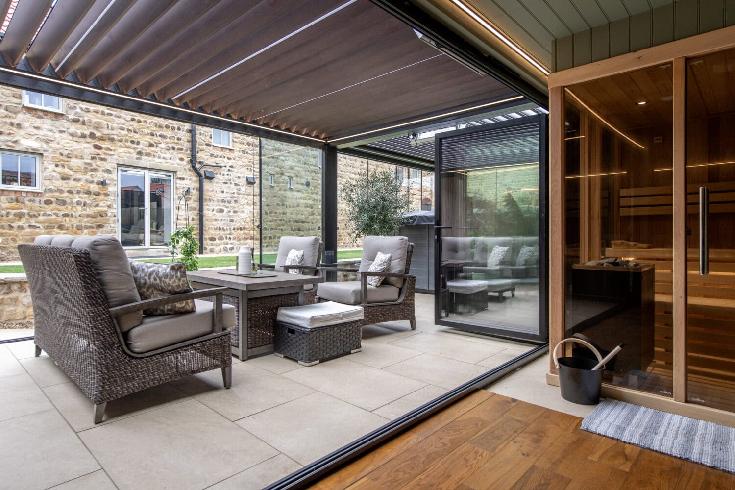 Contemporary outdoor patio featuring large bi-folding doors opening to a stylish seating area with wicker furniture and a glass roof.