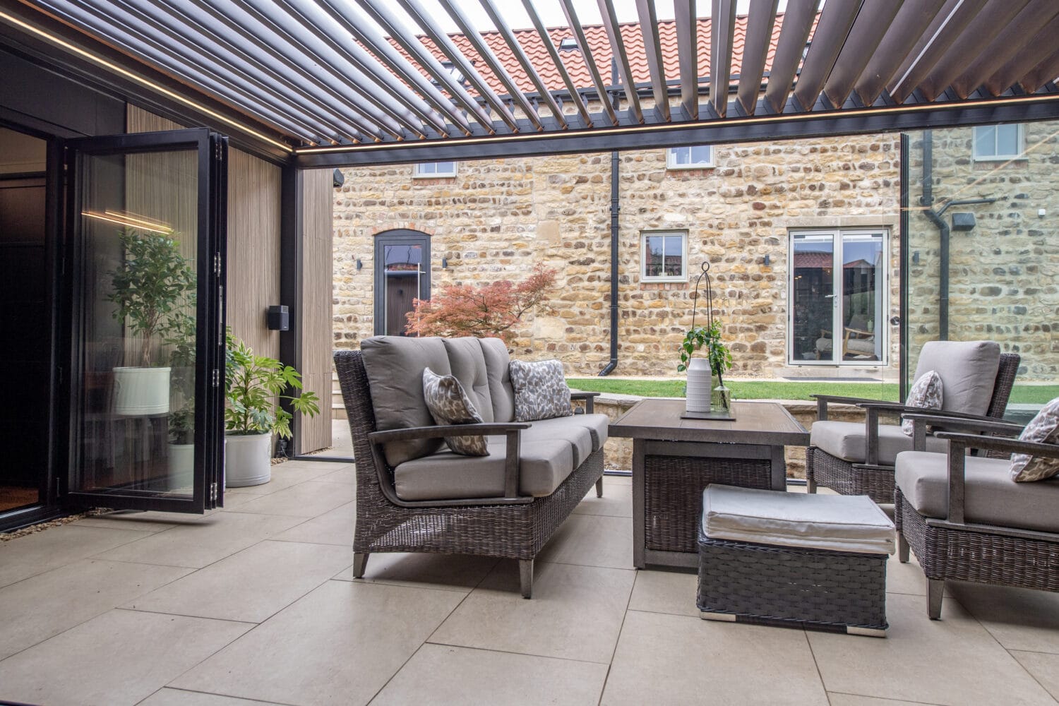Modern outdoor patio featuring large bi-folding doors opening to a garden, with comfortable seating and a stylish pergola overhead.