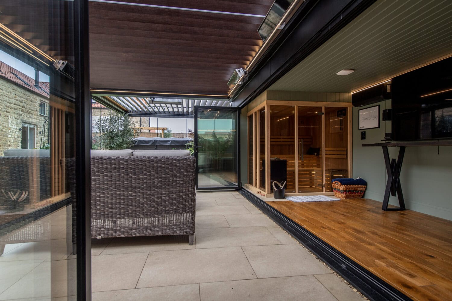Contemporary outdoor area featuring large bi-folding doors opening to a stylish patio with seating and a sauna.