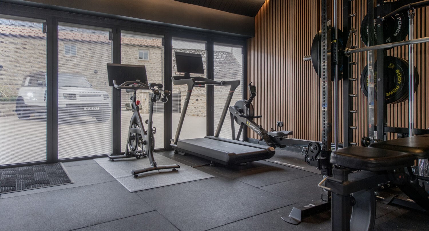 Interior of a modern gym with treadmill, exercise bike, and weightlifting equipment near large glass windows.