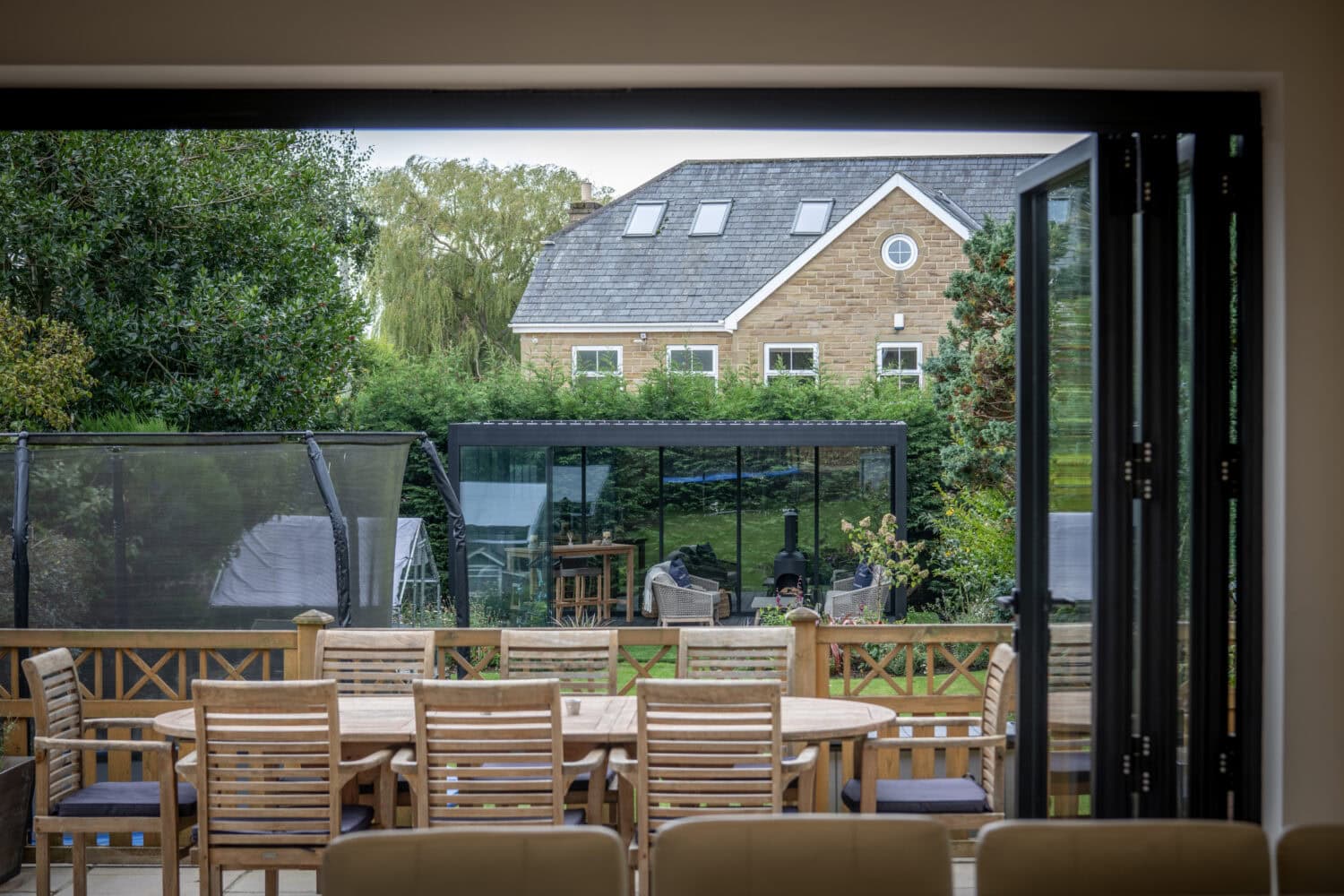 Modern bi-folding doors opening to a spacious outdoor patio with garden furniture and lush greenery, ideal for outdoor living and solar shading solutions.