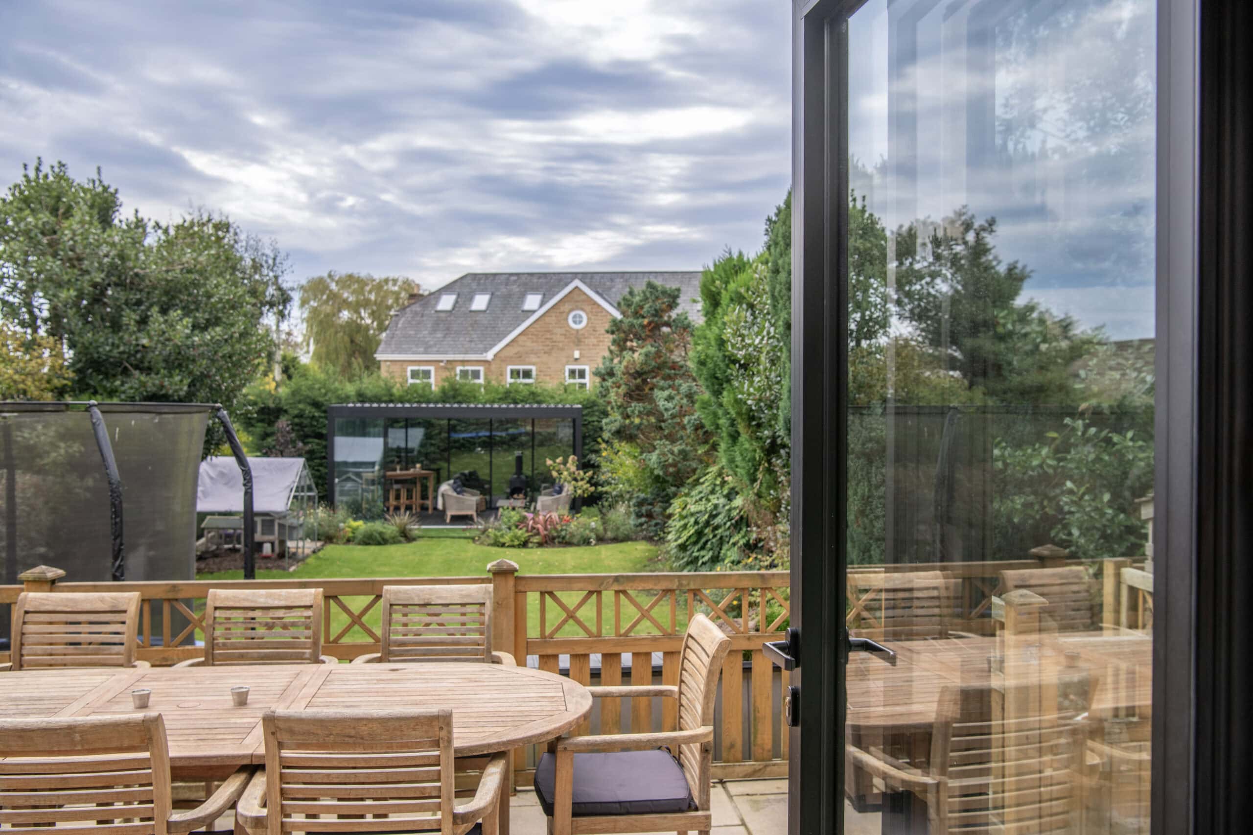 View of a garden with outdoor dining area and bi-folding doors leading to the patio, showcasing outdoor living and solar shading solutions.