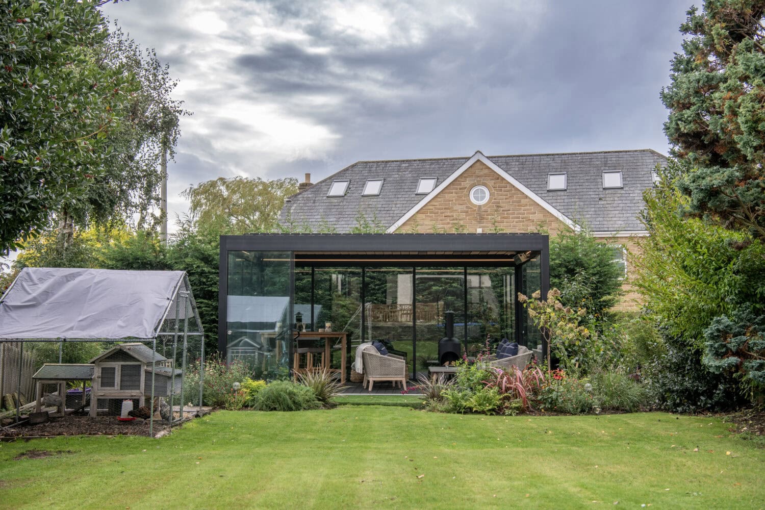 Contemporary glass extension with bi-folding doors opening to a lush garden, ideal for outdoor living and solar shading solutions.