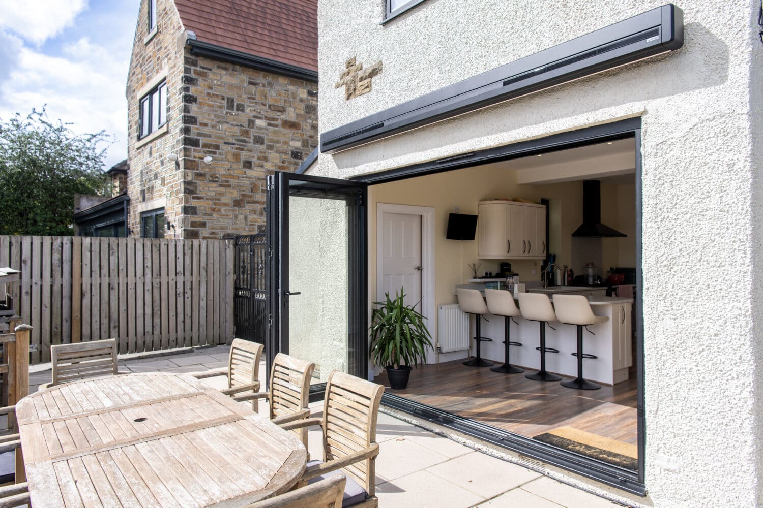 Modern bi-folding doors opening to a stylish outdoor patio with dining area, enhancing indoor-outdoor living space.