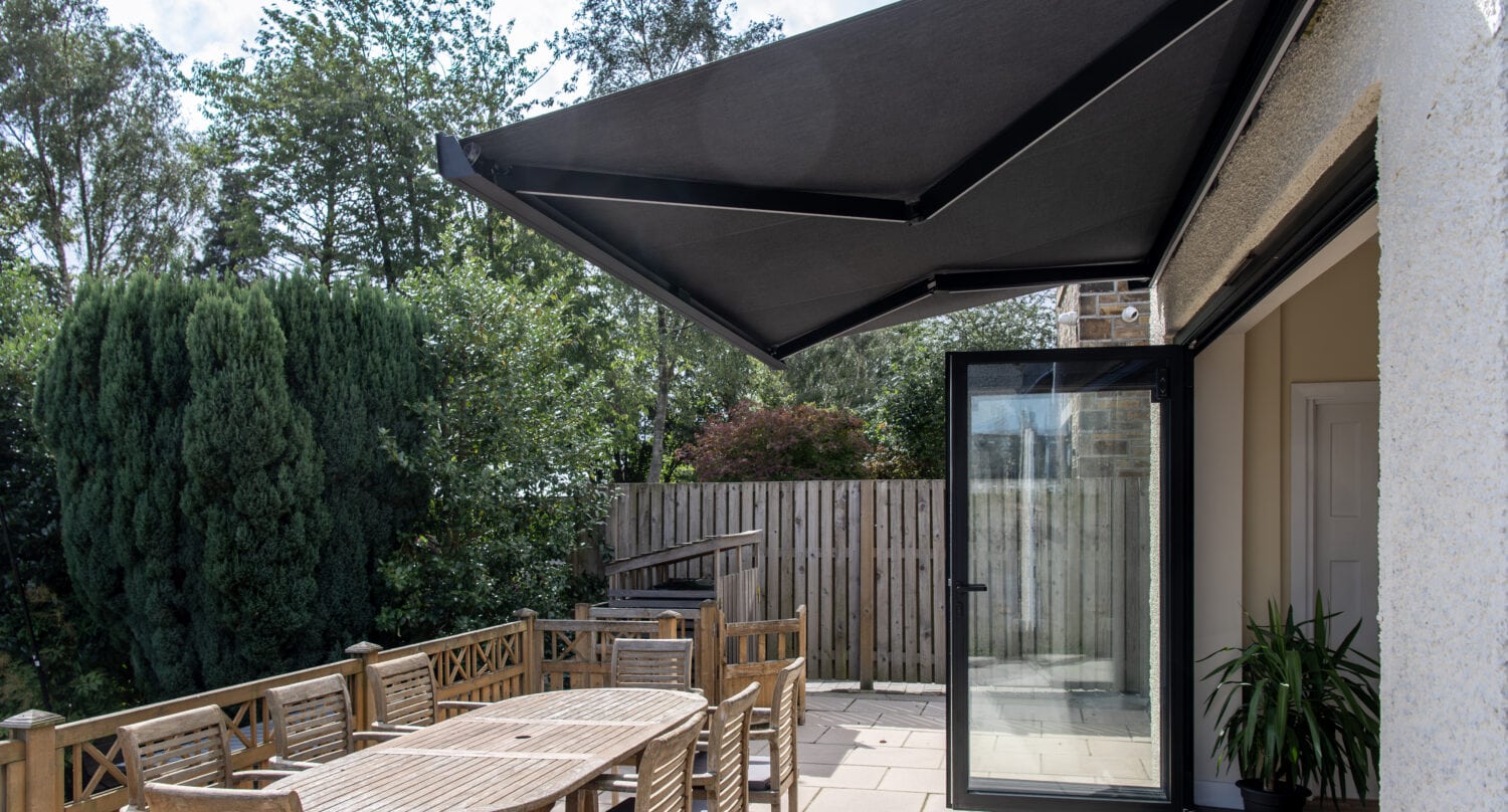 Modern outdoor patio featuring black bi-folding doors, a large canopy, and wooden dining furniture, ideal for outdoor living and solar shading solutions.