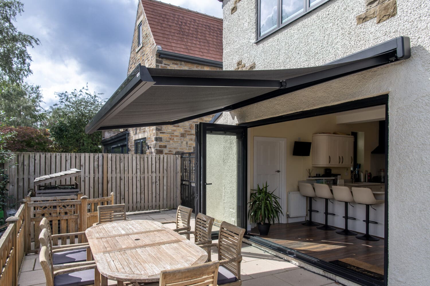 Modern outdoor patio with large bi-folding doors opening to a garden dining area, showcasing seamless indoor-outdoor living space with solar shading.