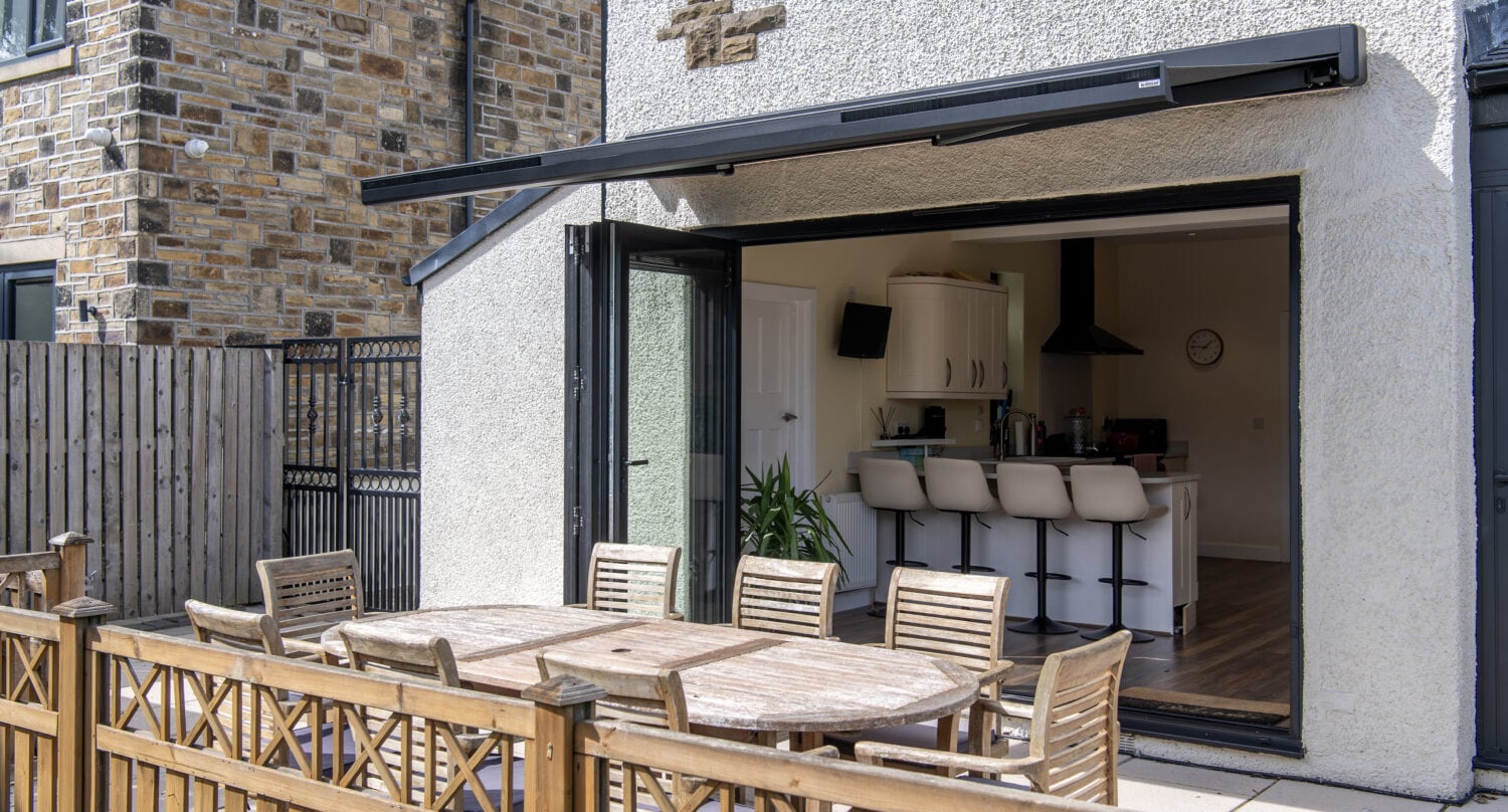 Modern outdoor living space featuring large black bi-folding doors opening to a patio with a dining area, ideal for seamless indoor-outdoor entertaining.